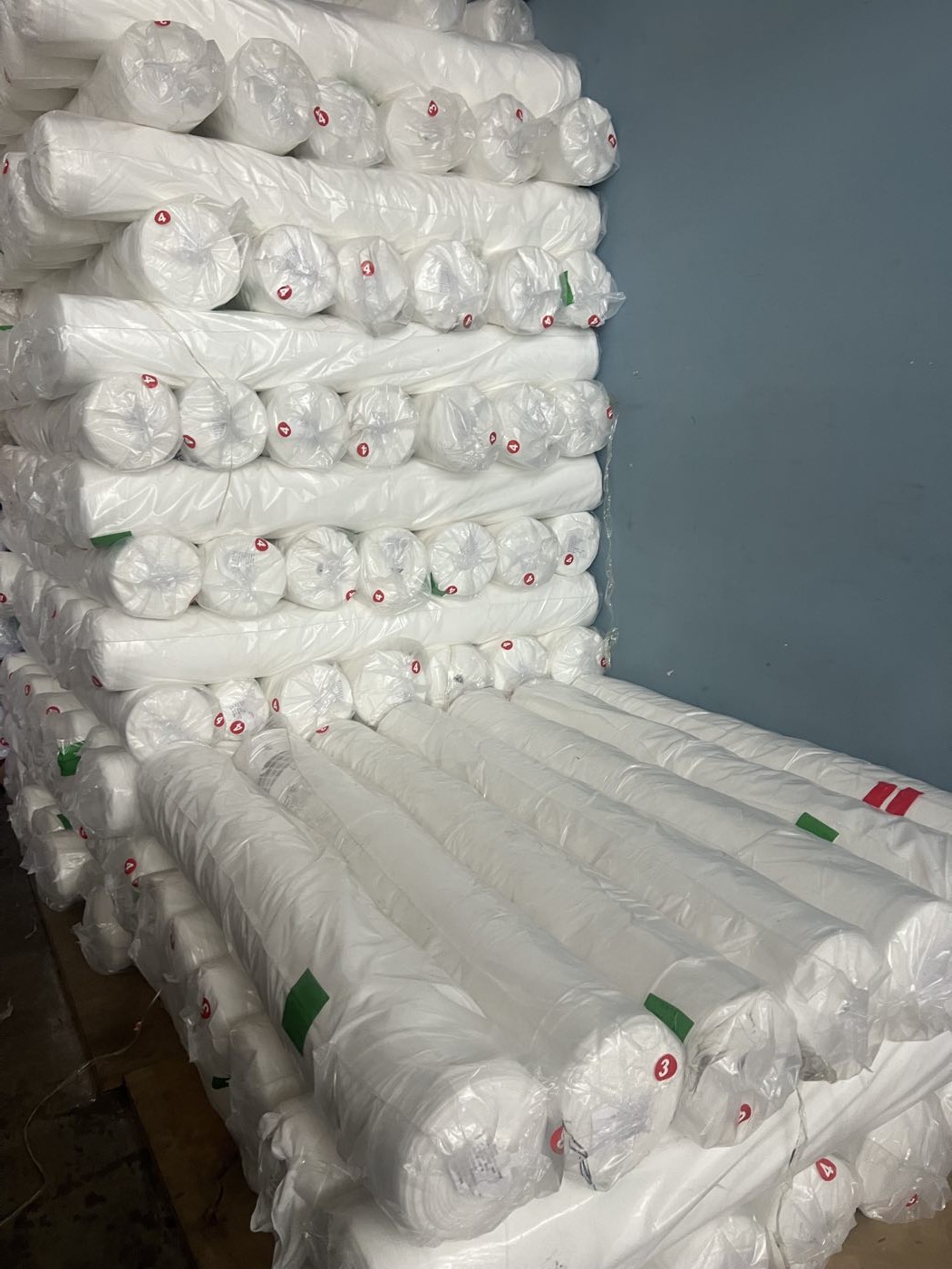 Stacked rolls of white polyester fabric held in stock